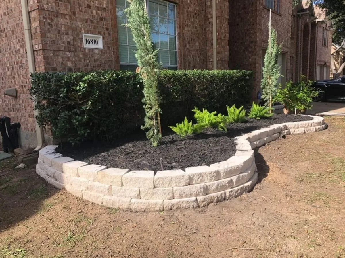Curved stone planter bed with new shrubs in front of a brick home