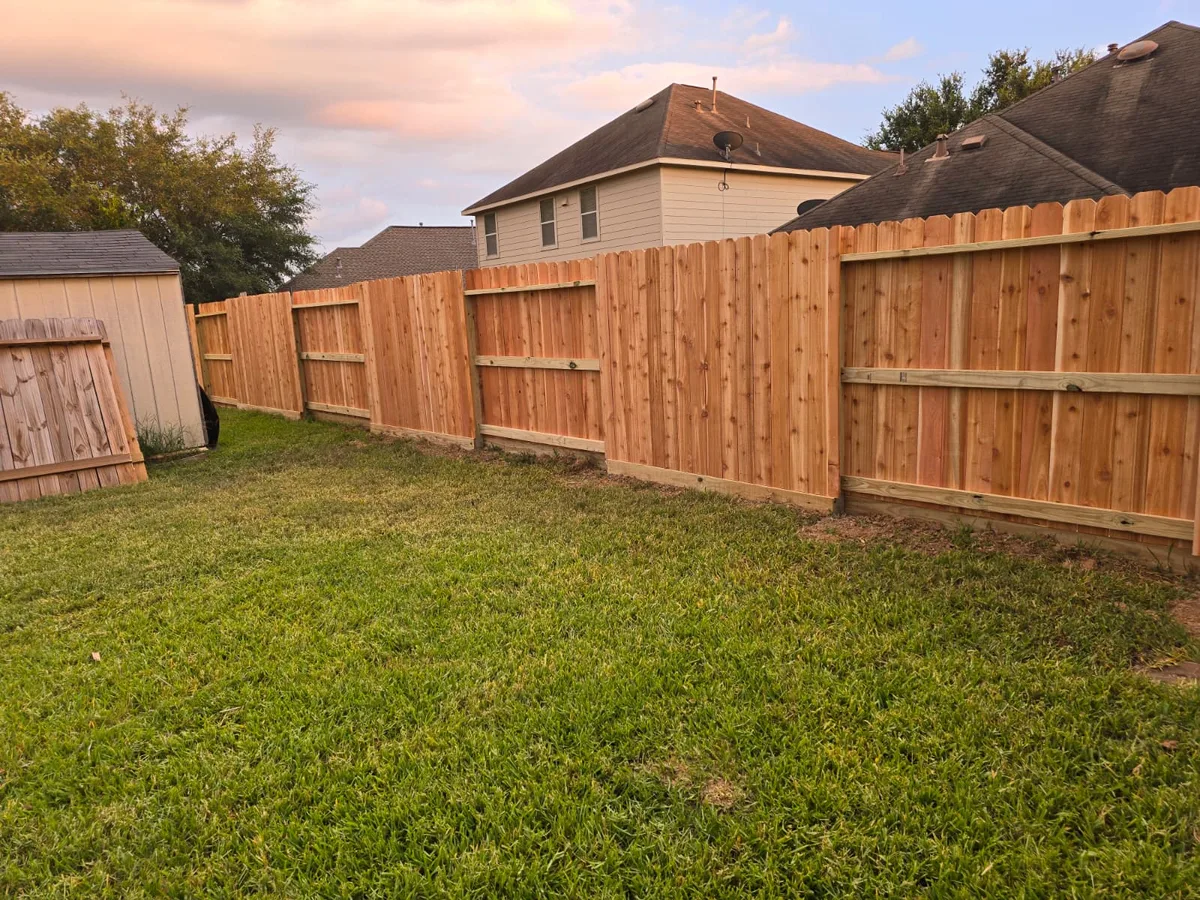 Wood privacy fence with a gate at the corner of a lawn