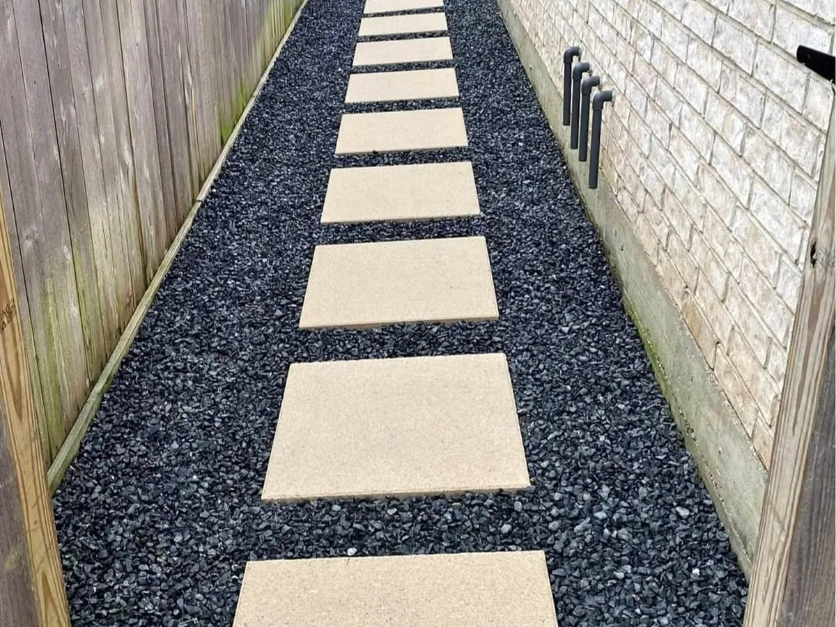 Concrete stepping pads set in black gravel along a side yard